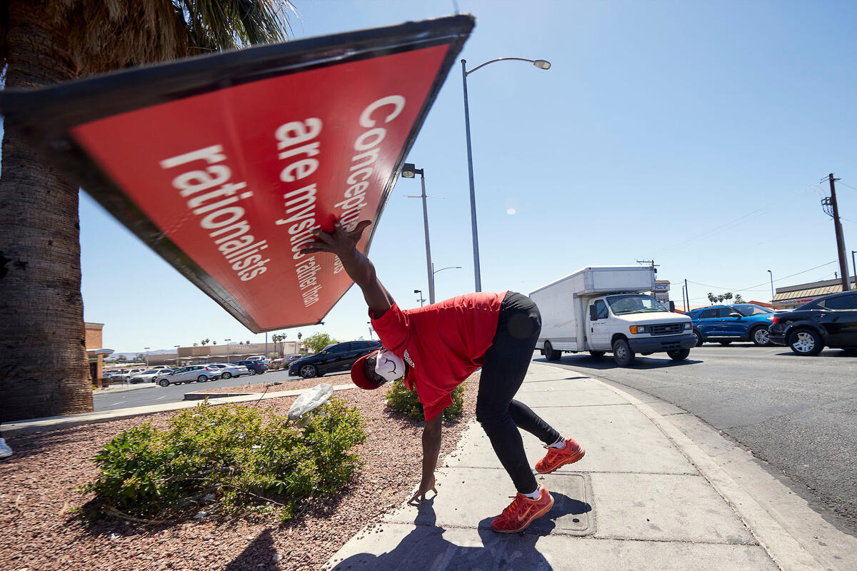 A man holds a sign over his head with one hand while the other is on the ground