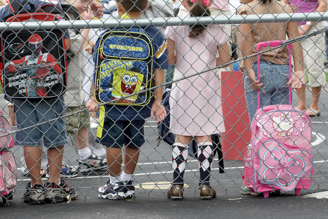 children standing on a playground with their backs to the camera and their backpacks visible
