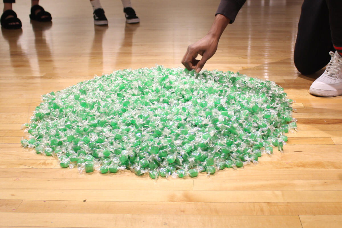 A hand picks up a piece of candy from a pile of it on the floor