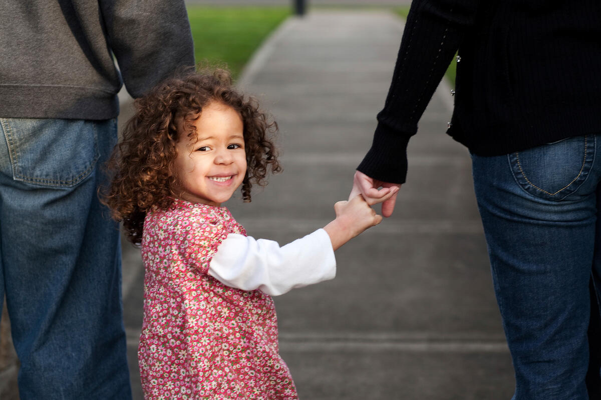 little girl looks back at camera while holding parents hands
