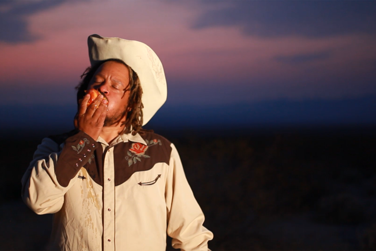 black man in cowboy hat eating fruit