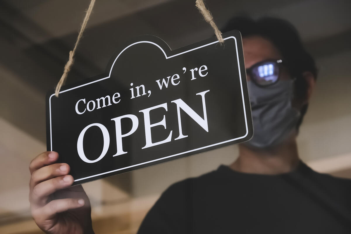 man wearing mask holds an "open" business sign