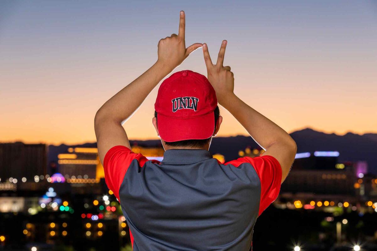 A student creates the letters L and V in front of a sunset and city skyline.