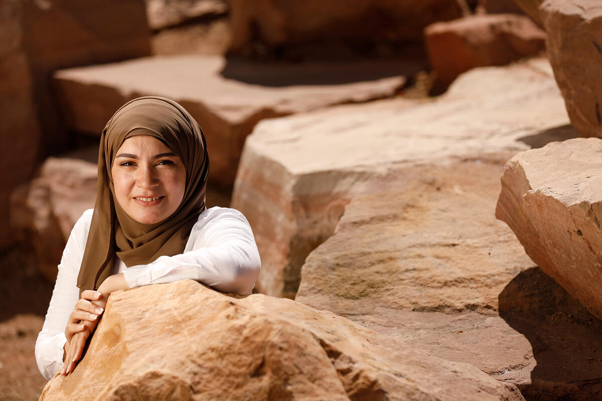 A woman wearing a veil over her head sitting among different rock formations.