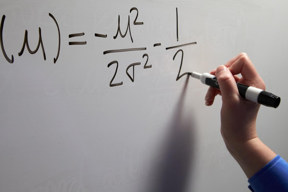 Closeup hand writing an equation on a white board