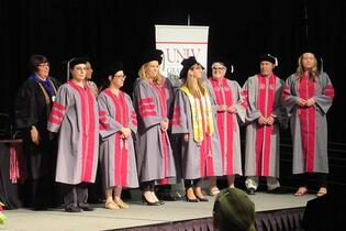 A group of graduates in gray and red gowns and caps.