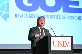 A speaker in front of a projection that reads the Nevada Governor's Office of Economic Development. The speaker's podium has the UNLV logo.