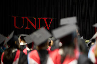 Graduate students at graduate commencement. Students are wearing black caps and gowns with red hoods.