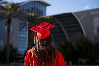 woman in red cap and gown facing toward building
