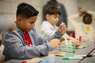 A young boy works on a science experiment by piping a liquid into a container.