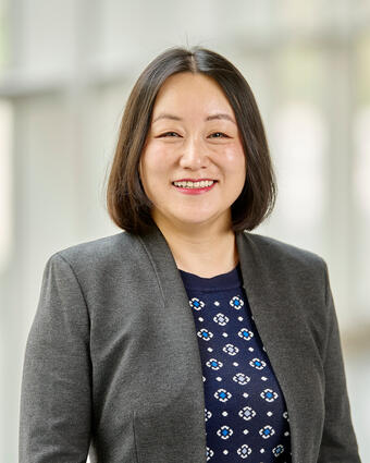 portrait of Yvonne Chen, wearing gray blazer, navy patterned top, and smiling