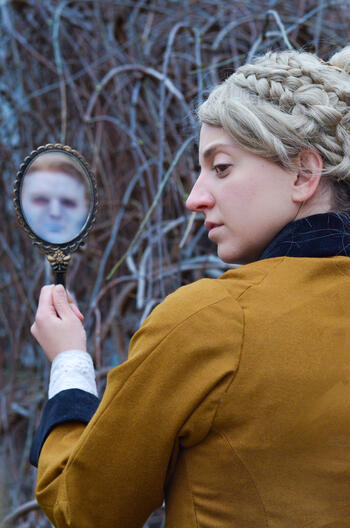 person looking over shoulder while holding small mirror