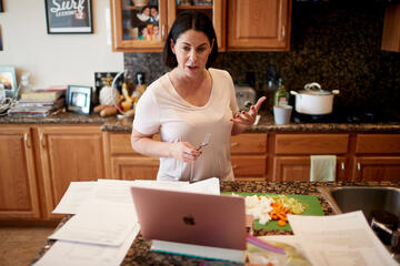 A woman gestures in her kitchen while teaching cooking lessons through videoconferencing