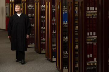 A woman in judge's robes walks through the stacks of a law library