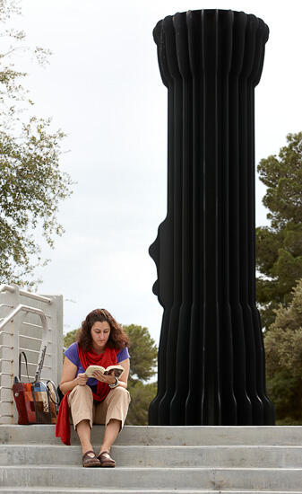 Woman reading a book at the top of stairs which lead to UNLV's sculpture called the "Flashlight".