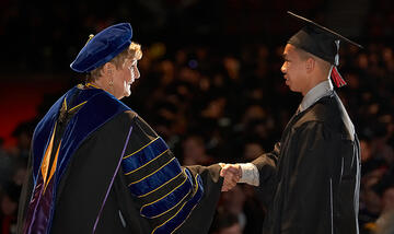 Mrs. Harter shaking the hand of a student during commencement as he walks by to receive his diploma.