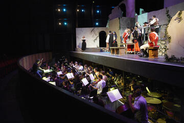 Student actors and orchestra conducting a play.