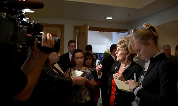 Mrs. Harter surrounded by reporters and cameras inside of a conference room.