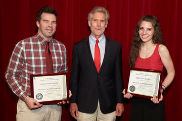 Three people standing and smiling for the camera. Two of which are holding their accepted awards.