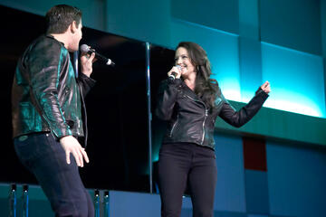 Two performers, on stage, holding and singing into their microphones.