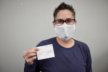 A person in a mask holds up their vaccine card to the camera.