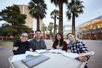 Students sit at an outdoor table reading books.