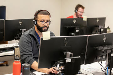 A man wearing a headset sits behind a computer