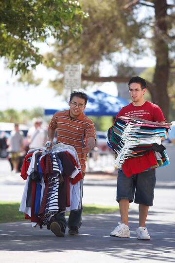Incoming students walking with their wardrobe in their hands.