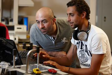 Two males stare into the screen of a laptop computer.