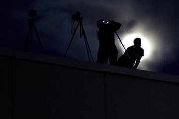 Silhouette of two photographers during the night with the full moon hiding behind the clouds.