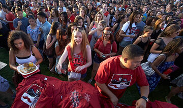 Crowd of people standing at a gathering. Two people, closest to camera, are handing out UNLV t-shirts.