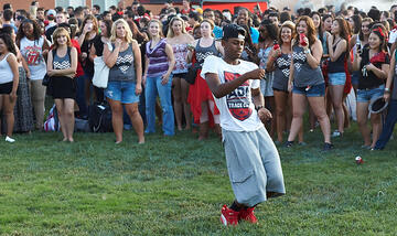 Young man dancing in the center of a crowd of people. Everyone in crowd is standing and watching him.