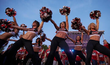 Ground front side view of the UNLV Rebel dancers. UNLV band is standing behind the group of dancers.