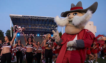 Front side view of Hey Reb mascot as he dances alongside the UNLV Rebel dancers who are all cheering behind him.