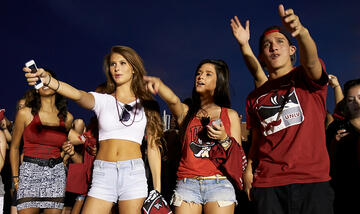 Three students at a pep rally, all pointing in different locations.