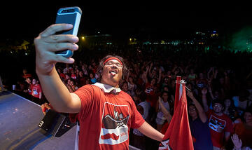 Student on stage taking a selfie of himself with the crowd of students in the background.