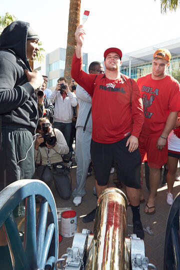 Student athlete holding up a paint brush with red paint on it while others stand around him.