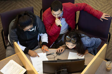 Three students look at a computer as they work on a group project.