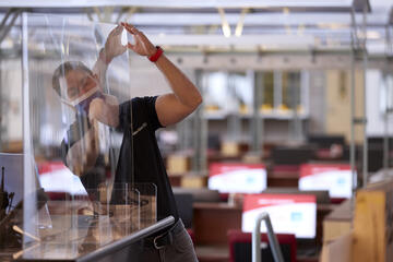 A man with a mask on installs a barrier in the UNLV Lied Library