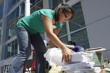 Woman picking up a piles of packets containing blank lined paper.