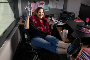 A woman holding a microphone kicks up her feet on her desk