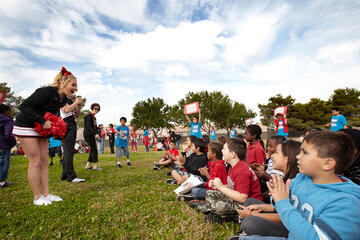 Runnin Rebels cheerleader ramping up a group of young multi-racial kids to cheer.
