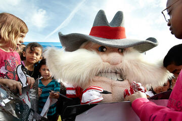 Hey Reb mascot signing kids' poster boards in a crowd of kids.