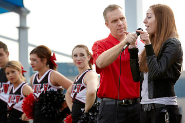 Man holding up a microphone to a young woman as she speaks to the crowd.