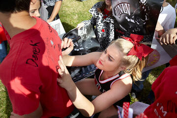 A Runnin Rebels cheerleader signing the back side tshirt of a kid.