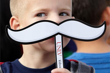 Close up of young boy holding a Hey Reb mustache against his face.