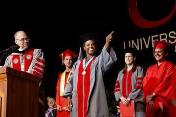 Student proudly points to audience during commencement.