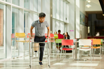 A student with his leg bandaged to simulate amputation uses a walker.