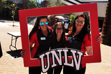 Three women hold a large frame bearing the letters "UNLV"