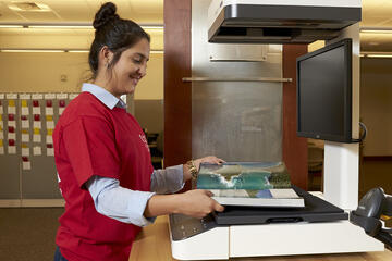 A student checking our a book at the library through an automated machine.